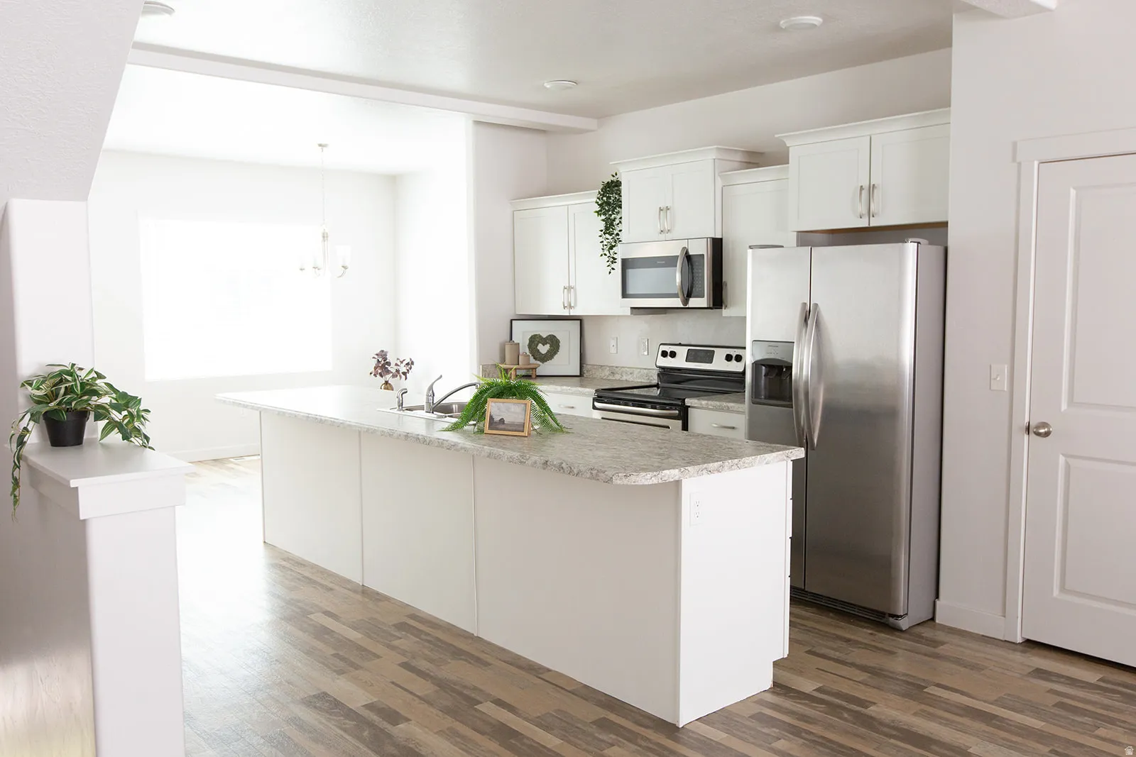 Open-concept kitchen featuring an island with a sink, white cabinetry, stainless steel appliances, and wood-finish flooring