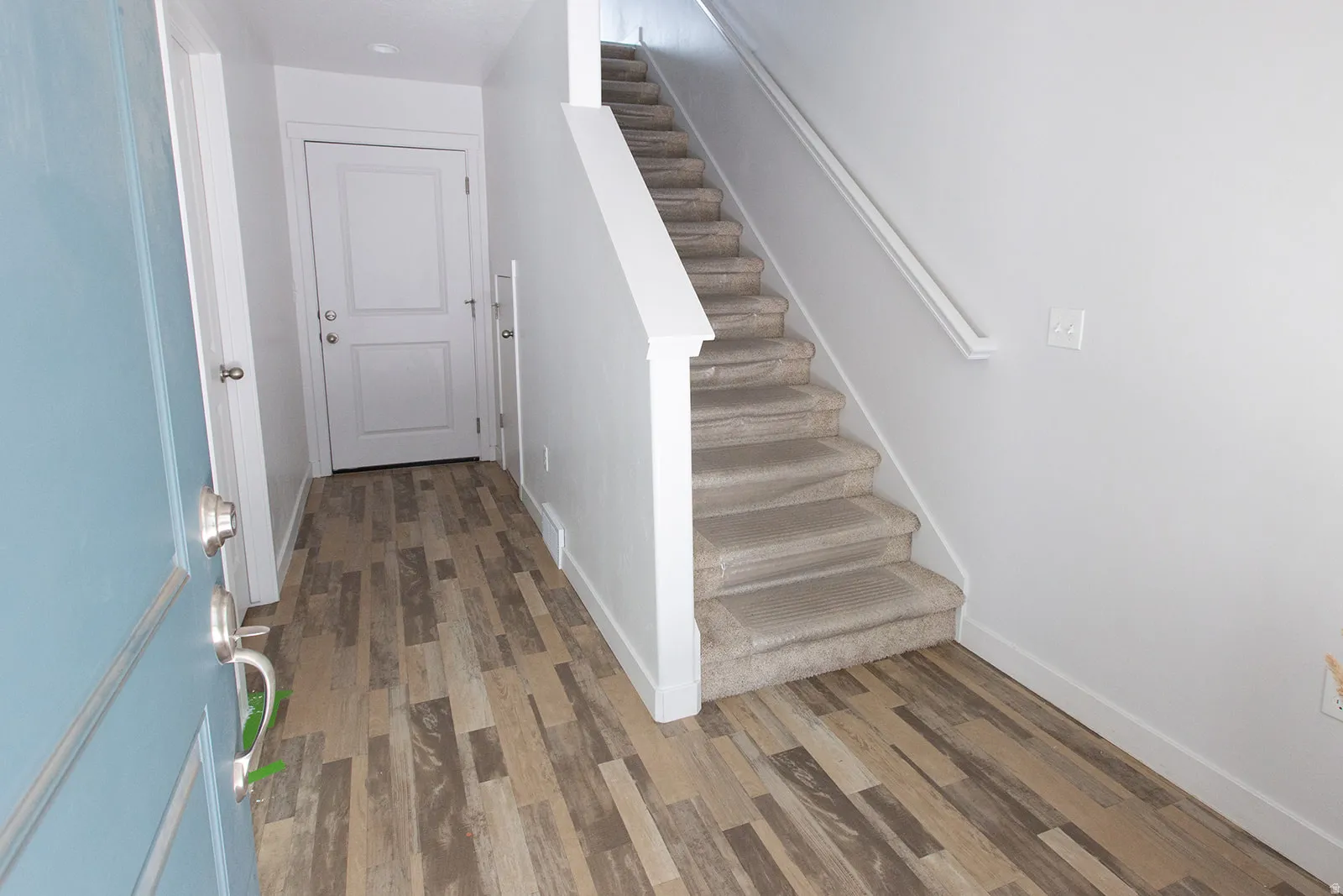 Entryway featuring wood-finish flooring, a light blue door with brushed nickel hardware, a white interior door, and a carpeted staircase with a white railing