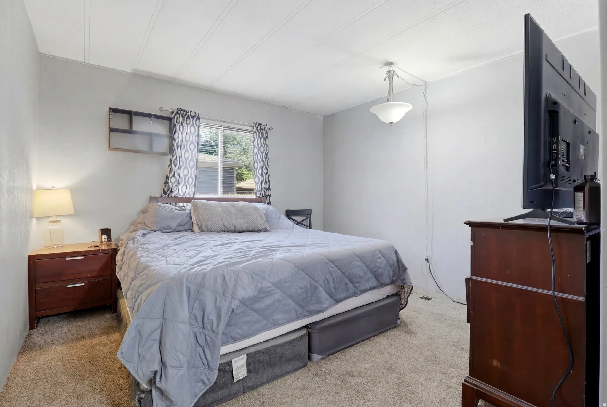 Carpeted room featuring a window with patterned drapes, a light gray wall finish, and a ceiling-mounted light fixture