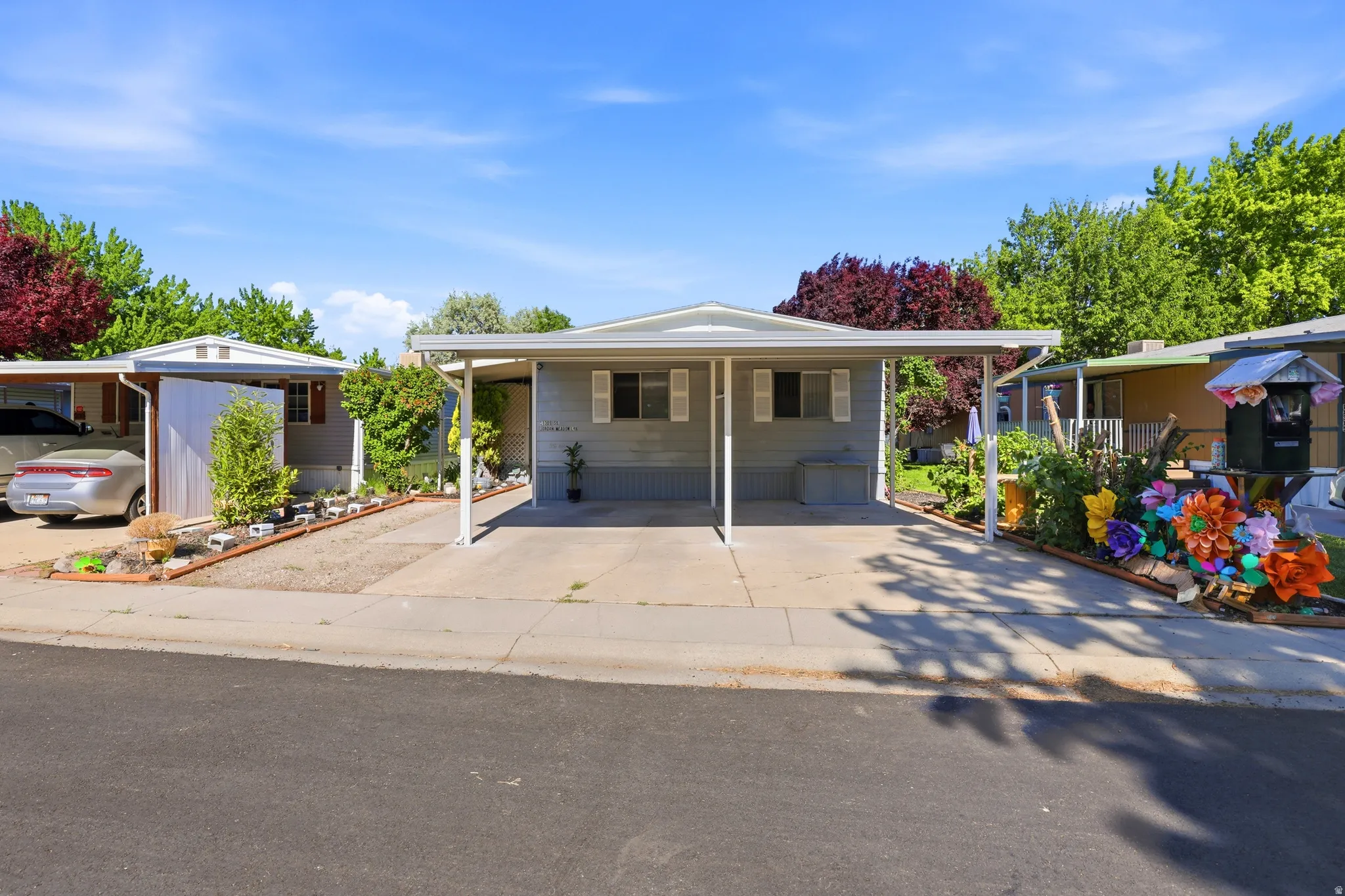 Manufactured home featuring light gray siding with white trim, a double carport, and a low-maintenance front yard