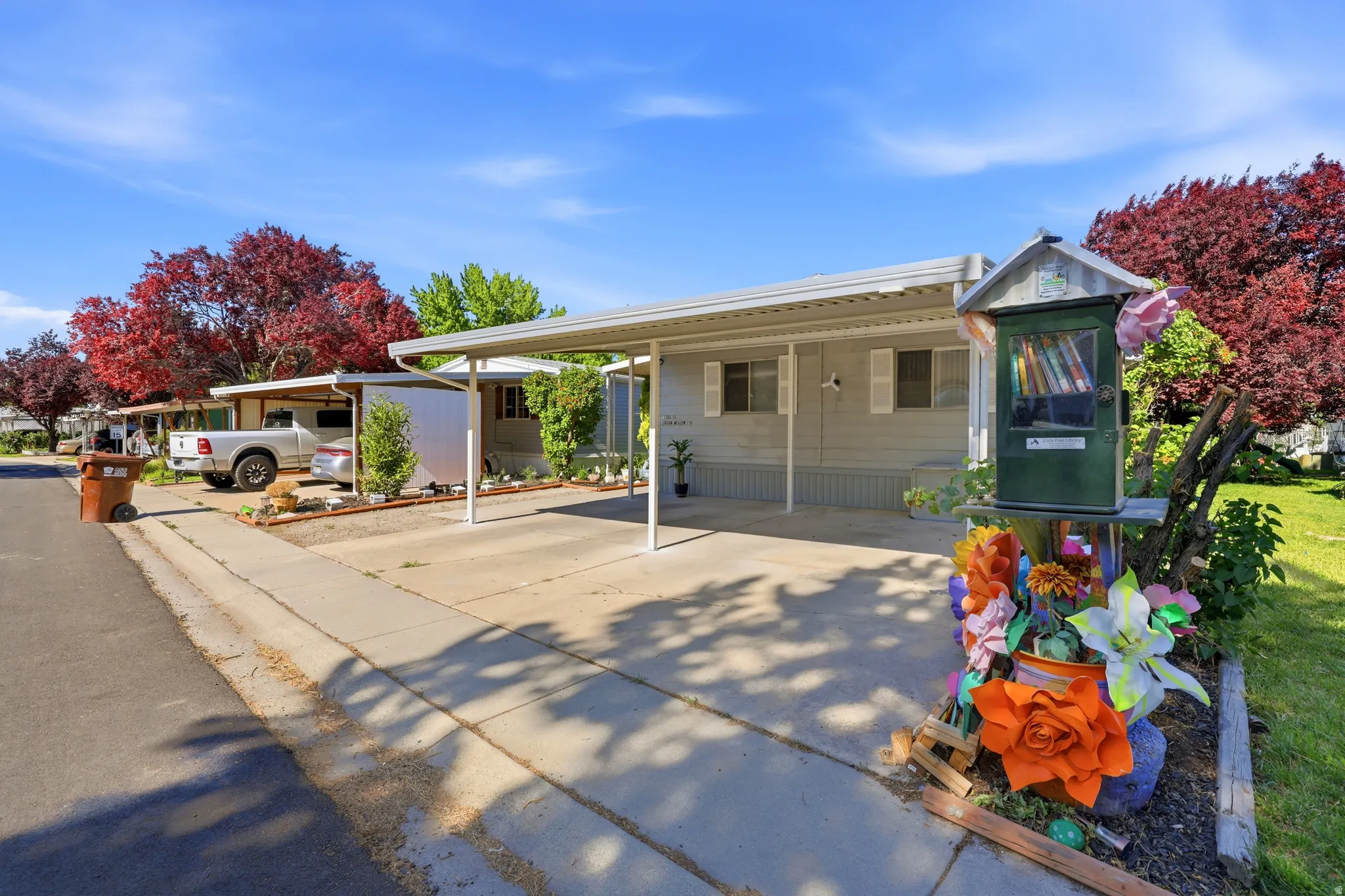 Property featuring a paved driveway with a carport, mature red-leafed trees, and a decorative front yard garden area