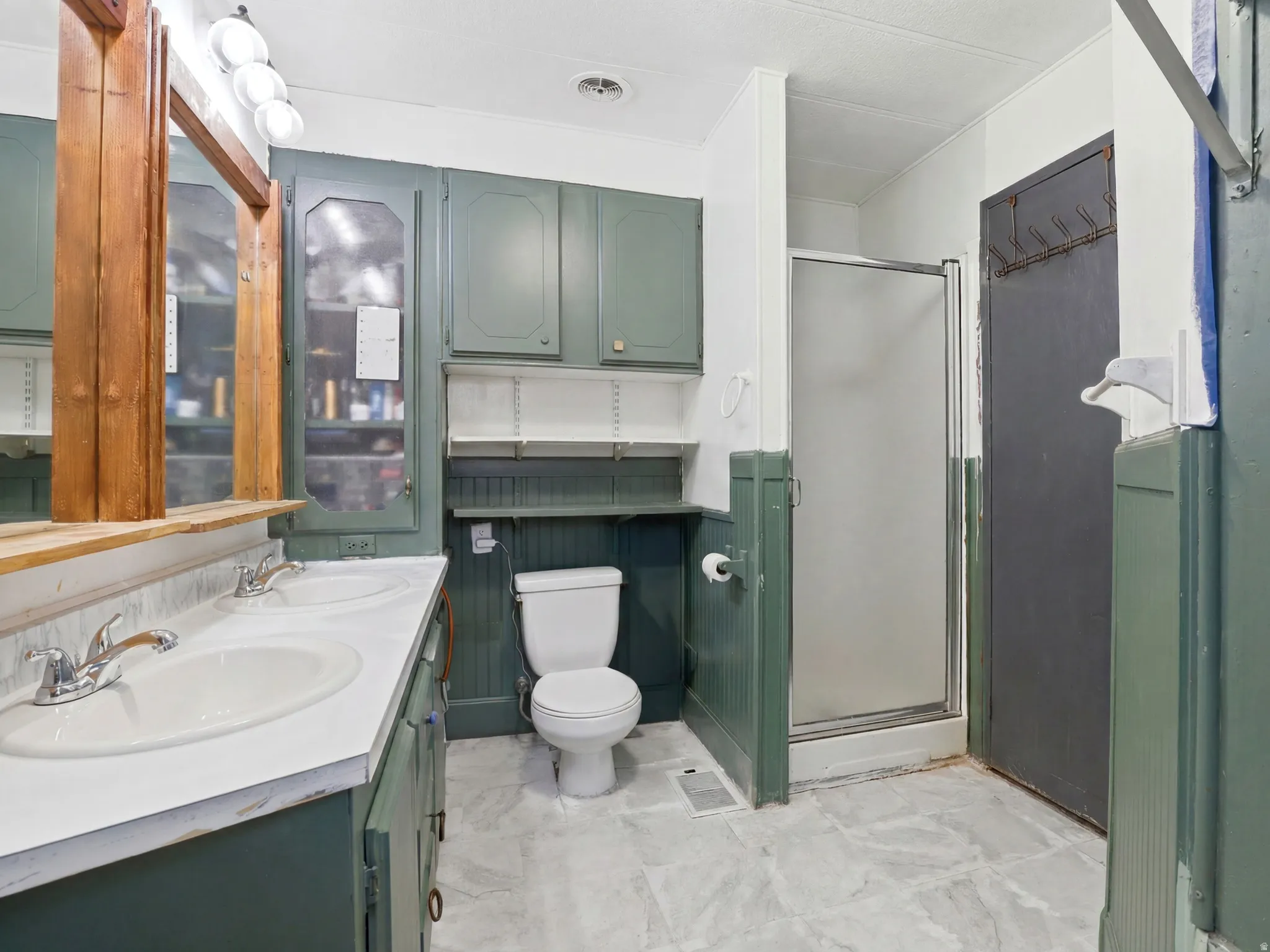 Bathroom featuring a double vanity with white countertops, a single toilet, a standing shower with a glass enclosure, and overhead cabinetry