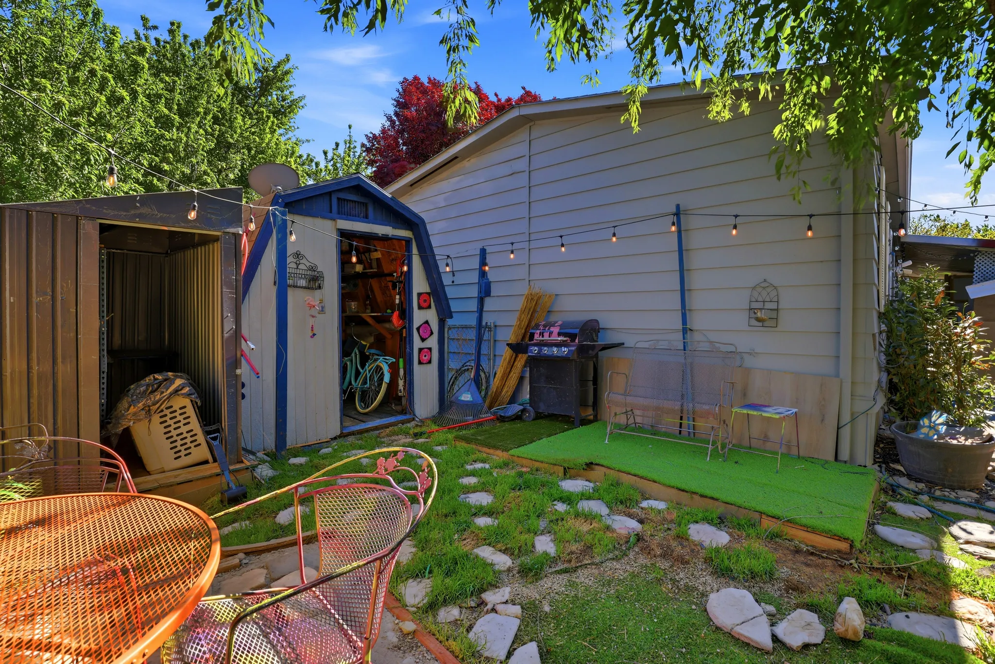 Backyard space featuring two storage sheds, string lighting, and a stepped green artificial turf area