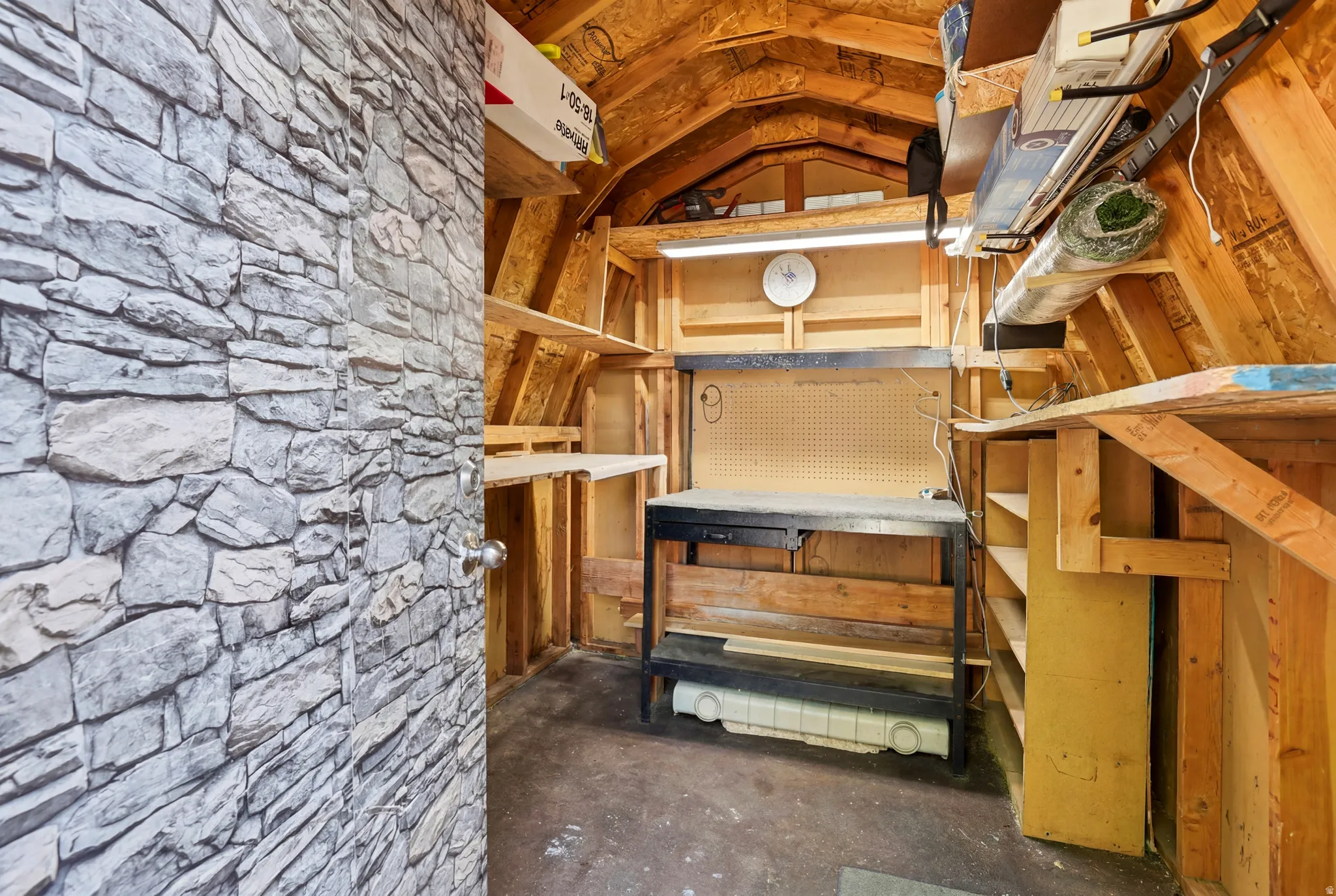 Utility shed interior featuring exposed wood framing, built-in shelving, a workbench, and a pegboard wall