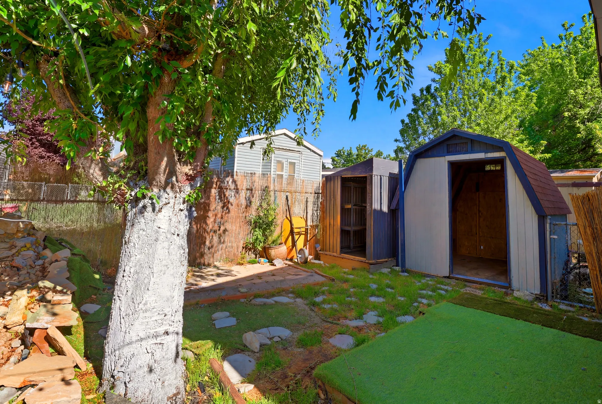 Backyard featuring two storage sheds, a mature tree, stone pathway, and a green turf area