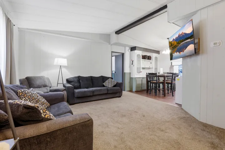 Open-concept living area with neutral carpeting, white paneled walls, and a recessed ceiling