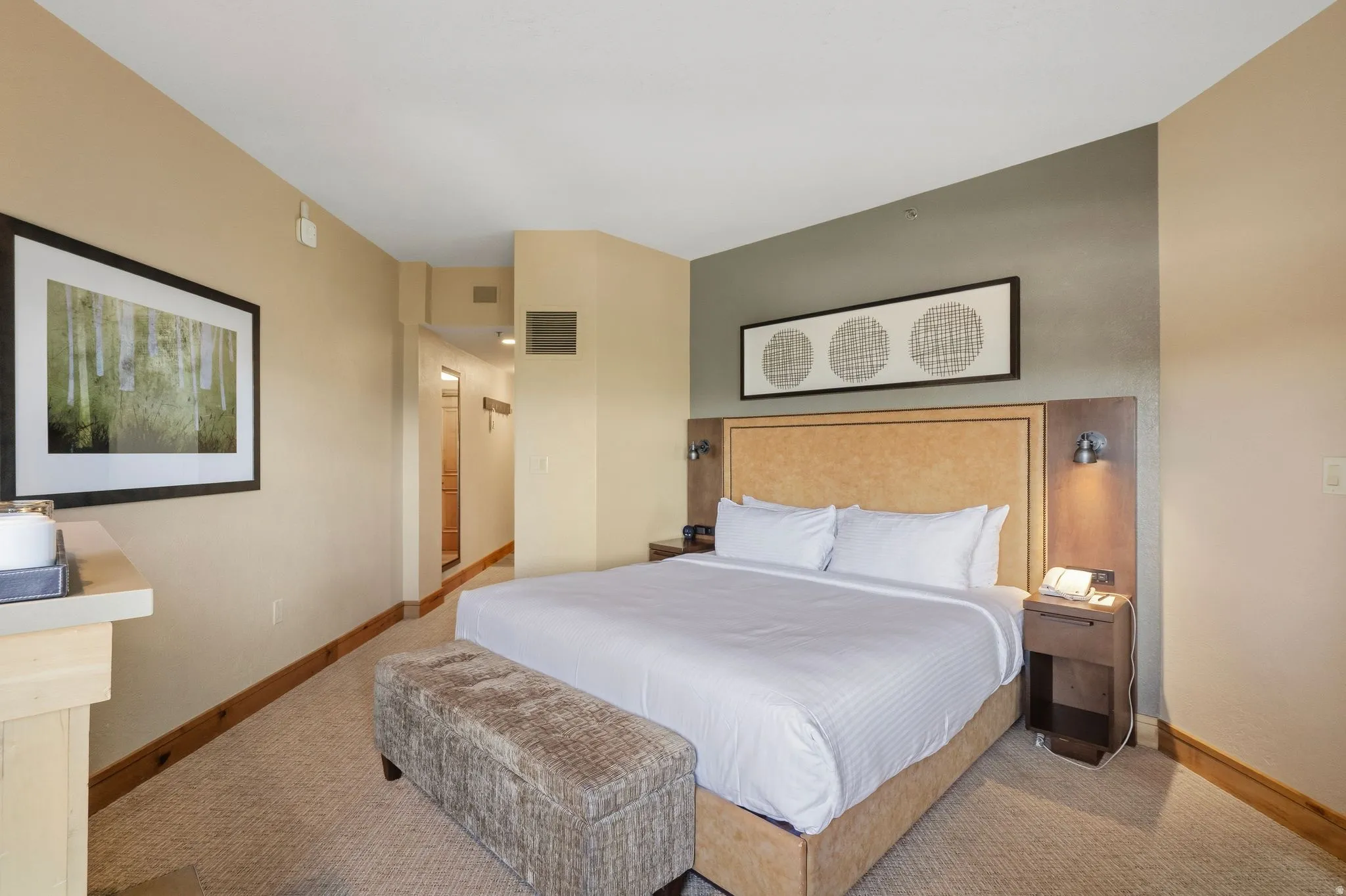 Carpeted room featuring a large bed with an upholstered headboard, integrated sconce lighting, and a built-in nightstand