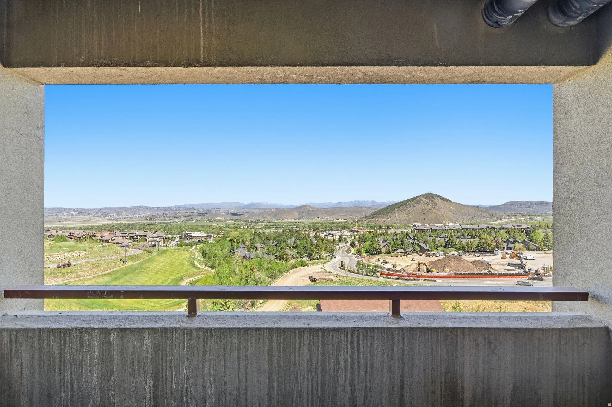 Sweeping mountain and valley scenery with a community backdrop, framed by a concrete balcony with a metal railing