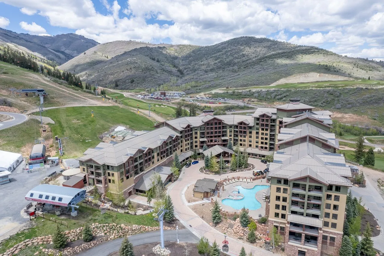 Multi-story resort-style building with a terraced facade, featuring extensive balconies, an outdoor swimming pool, and a ski lift structure