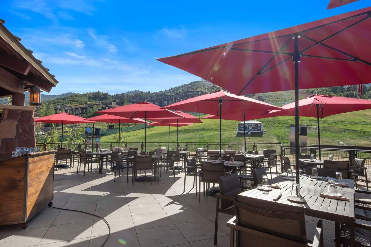 Expansive outdoor patio featuring a stone and wood-clad architectural element, multiple dining tables, a tile surface, and metal railings