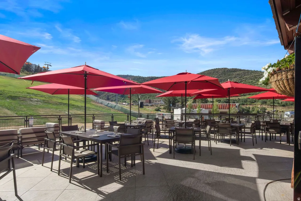 Spacious outdoor patio featuring multiple red patio umbrellas, a tile-paved surface, and a metal railing