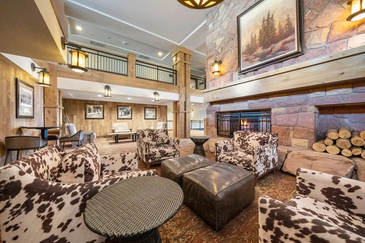 Spacious common area featuring a grand stone fireplace with a substantial timber mantel, wood paneling, and a high ceiling with recessed lighting