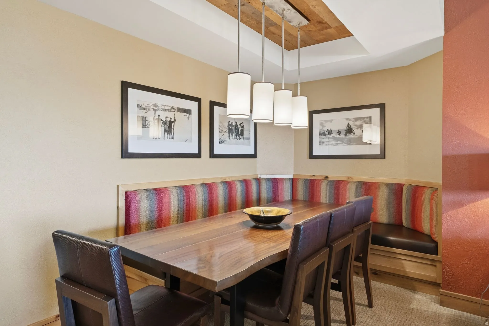 Dining area featuring a built-in corner banquette with vibrant striped upholstery, a rectangular wood dining table, and four pendant lights