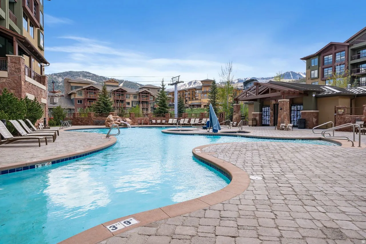 Curved swimming pool with an integrated hot tub and stone waterfall feature, surrounded by a paver patio