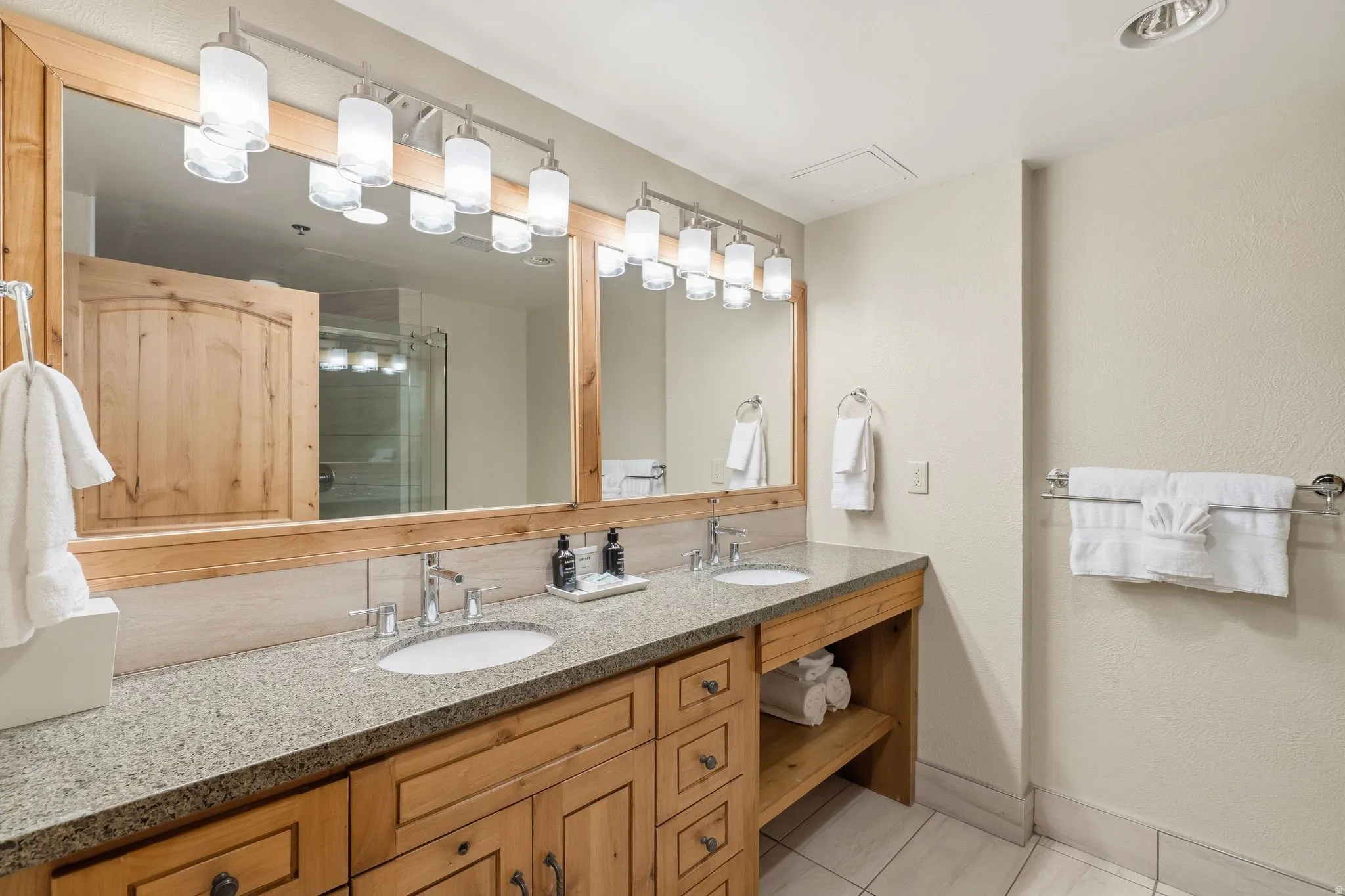 Double vanity featuring light wood cabinetry, stone-finish countertop, and undermount sinks
