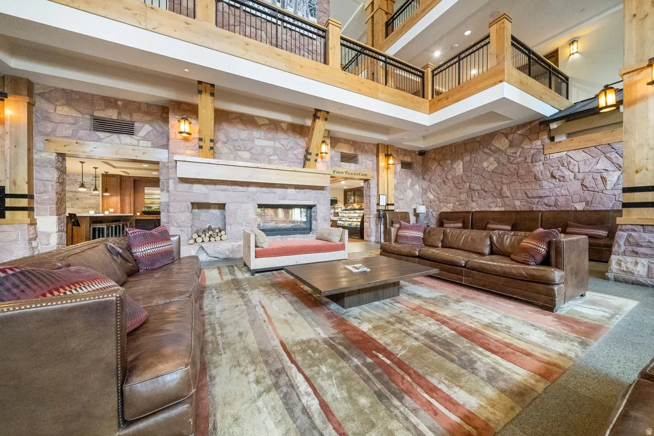 Grand two-story living area featuring stone accent walls, exposed wood beams, a built-in fireplace, and a second-story overlook with metal railings