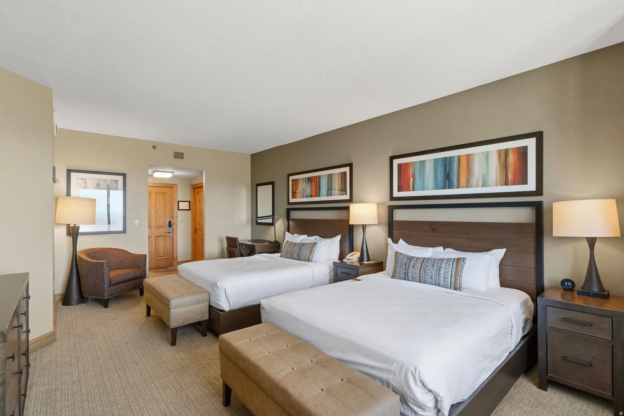 Carpeted bedroom featuring two beds with dark wood headboards, framed artwork, a desk area, and a built-in closet with a wood door
