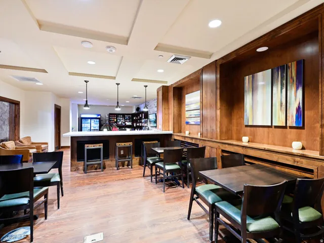 Spacious common area featuring wood-finish flooring, a full-service bar with pendant lighting, recessed ceiling panels, and extensive wood paneling with integrated shelving