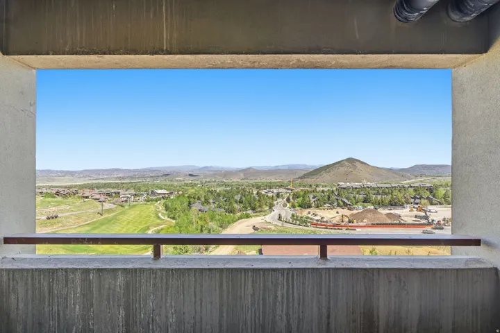 Sweeping mountain and valley scenery with a community backdrop, framed by a concrete balcony with a metal railing