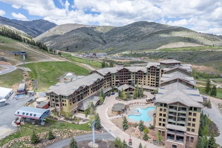 Multi-story resort-style building with a terraced facade, featuring extensive balconies, an outdoor swimming pool, and a ski lift structure
