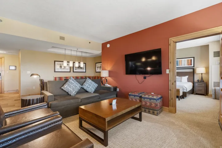Living area with carpet flooring, a mounted flat-screen television, and a wood-finish coffee table