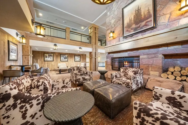 Spacious common area featuring a grand stone fireplace with a substantial timber mantel, wood paneling, and a high ceiling with recessed lighting