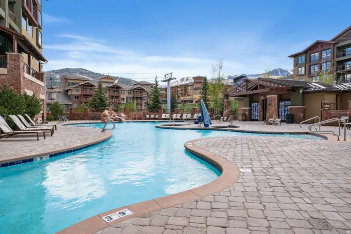 Curved swimming pool with an integrated hot tub and stone waterfall feature, surrounded by a paver patio