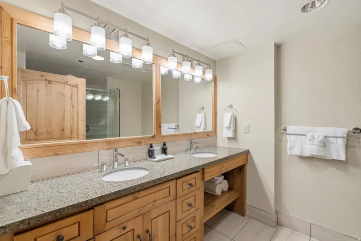 Double vanity featuring light wood cabinetry, stone-finish countertop, and undermount sinks