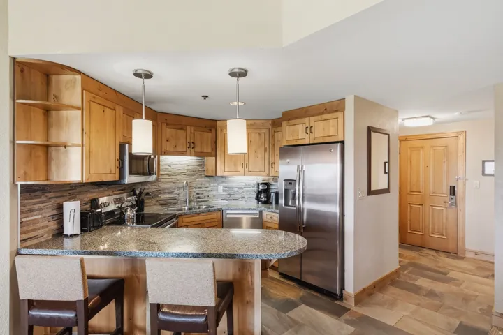 Kitchen featuring wood cabinetry, stainless steel appliances, a stone countertop island with seating, a tile backsplash, and recessed lighting