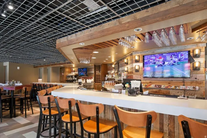 Expansive bar area featuring a white countertop, wood-finish wall paneling, and a grid-style ceiling