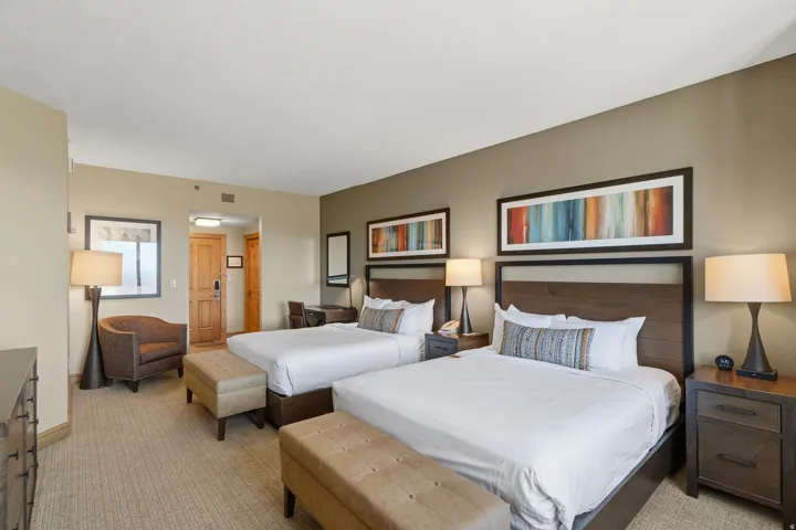 Carpeted bedroom featuring two beds with dark wood headboards, framed artwork, a desk area, and a built-in closet with a wood door