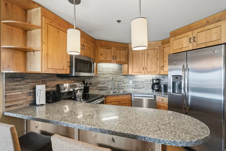 Kitchen featuring granite countertops, stainless steel appliances, wood cabinetry, stone-finish backsplash, and pendant lighting