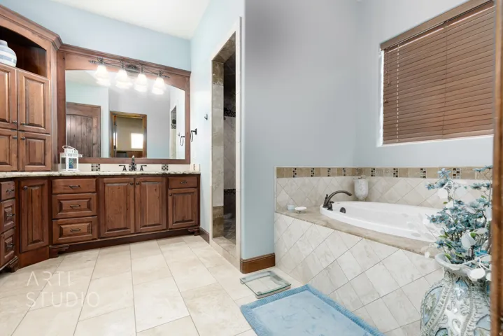 Spacious bathroom featuring a built-in soaking tub with tiled surround, a large vanity with wood cabinetry and dual sinks, a framed mirror, and a separate shower enclosure
