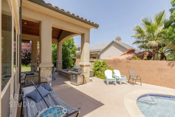 Outdoor living space featuring a covered patio with a wood-finish ceiling, stone-clad columns, and a built-in outdoor grill