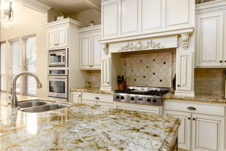 Kitchen featuring a dual basin sink, stainless steel appliances, ornate range hood, extensive cabinetry, and stone countertops