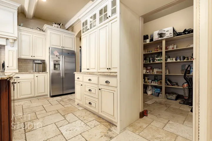 Kitchen featuring cream-colored cabinetry, stone tile flooring, a built-in stainless steel refrigerator, and a walk-in pantry with extensive shelving
