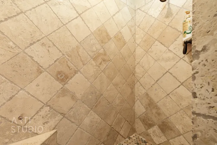 Shower enclosure featuring natural stone diamond-patterned wall tiles and a mosaic pebble-tiled floor