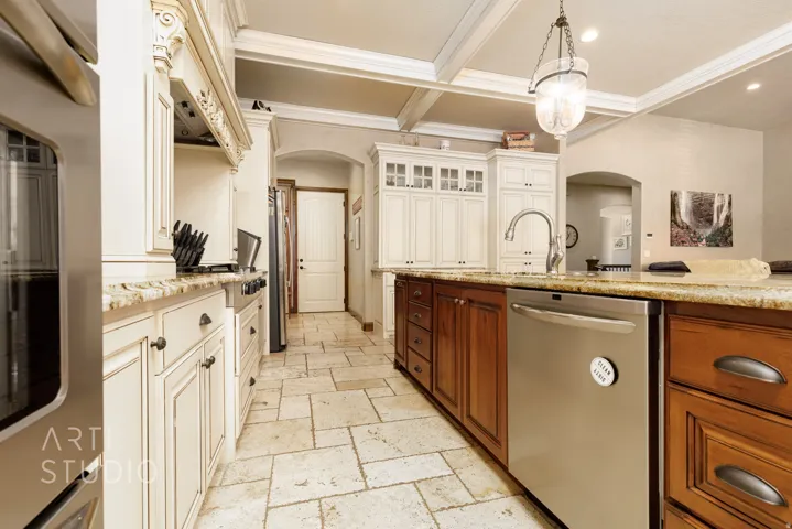 Gourmet kitchen featuring a large central island with integrated stainless steel dishwasher, stone countertops, and a double basin sink with a gooseneck faucet