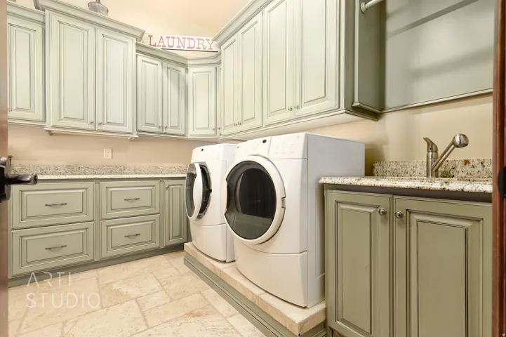 Dedicated laundry area featuring extensive cabinetry, stone-finish countertops, and an integrated utility sink