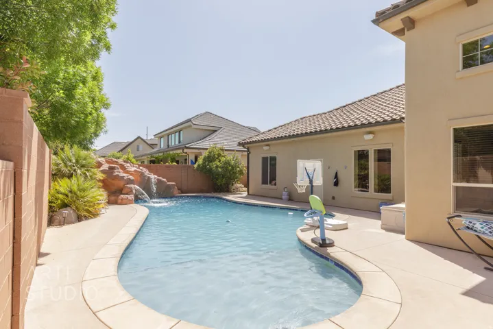 Curved swimming pool with a rock waterfall feature, complemented by surrounding concrete decking and stucco exterior walls