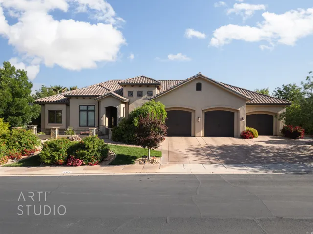 Stucco exterior with a tiled roof, featuring arched garage doors, a concrete driveway, and established landscaping