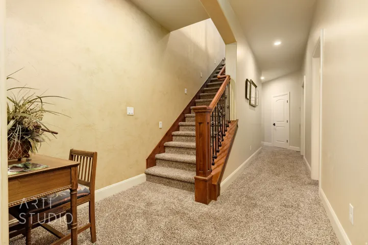 Staircase featuring wood newel posts, wrought iron balusters, and carpeted treads