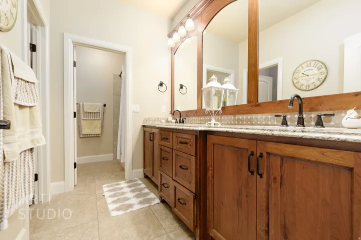 Double vanity featuring wood cabinetry, granite countertops, and dual wall-mounted mirrors