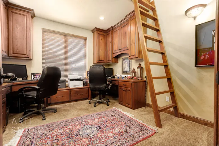 Dedicated office space featuring extensive built-in cabinetry, integrated desk areas, and a rolling wooden ladder