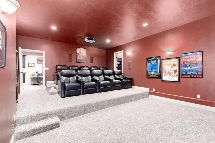 Dedicated home theater featuring tiered seating, plush carpeting, a ceiling-mounted projector, and integrated wall speakers