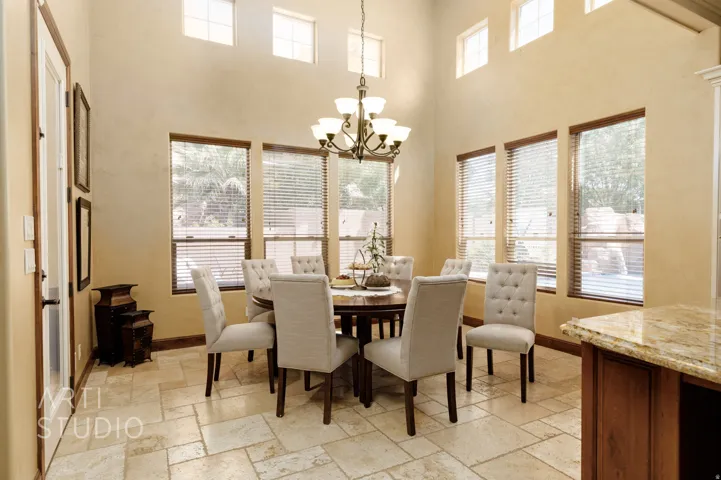 Dining area featuring high ceilings, light stone-look tile flooring, and multiple windows with wood-finish blinds
