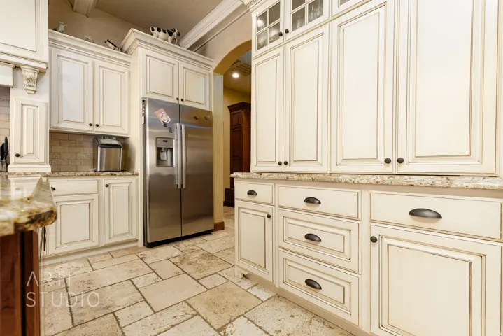 Kitchen featuring extensive cream-colored cabinetry with dark hardware, stone tile flooring, stainless steel refrigerator, and granite countertops