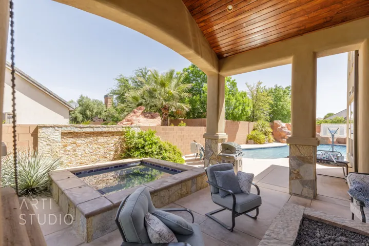 Covered patio featuring a wood-panel ceiling, stone-clad columns, an integrated spa, and a built-in fire pit
