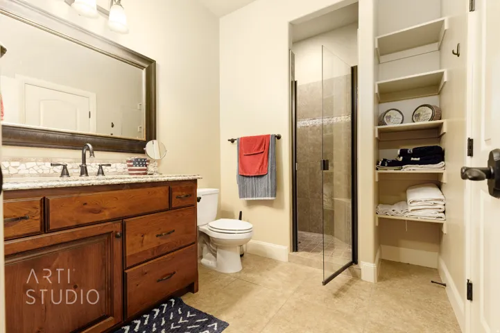 Bathroom featuring a wood-finish vanity with a granite-style countertop, undermount sink, and mosaic tile backsplash