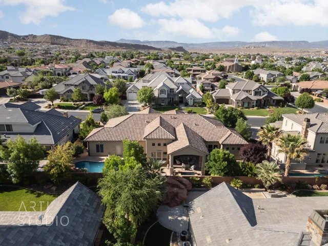 Aerial perspective of a residential neighborhood featuring a property with a private swimming pool, covered patio, and mature landscaping